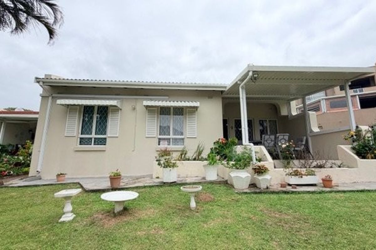 Rear view of the townhouse featuring a covered patio area, security shutters on windows, and a landscaped garden with paved sections.