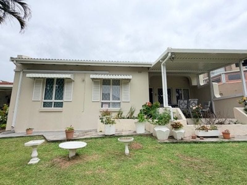 Rear view of the townhouse featuring a covered patio area, security shutters on windows, and a landscaped garden with paved sections.