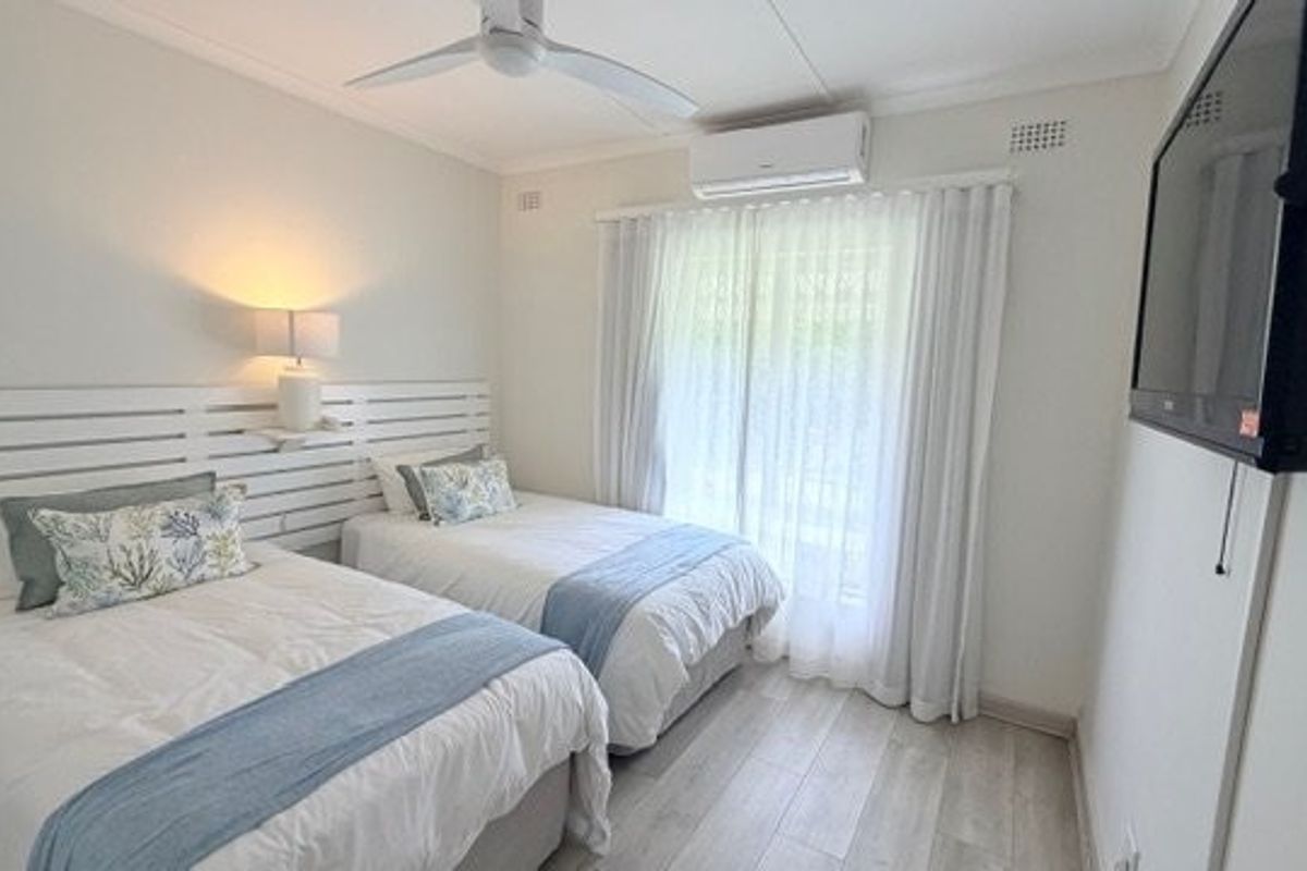 A well-maintained bedroom featuring light-toned laminate flooring, a ceiling fan, and a split-system air conditioner, with direct access to an outdoor area.
