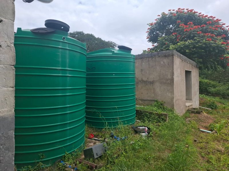 Outdoor utility area featuring two large green water storage tanks and a small concrete pump house structure on the farm property.