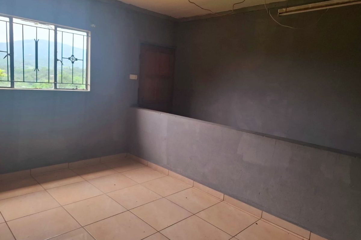 An empty, unfinished living area featuring tiled flooring, security bars on the window, and a half-height partition wall with exposed electrical wiring.