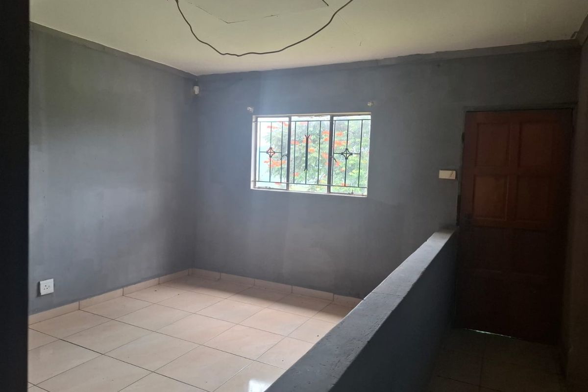 An empty bedroom featuring tiled flooring, a timber door, and security bars on the window, currently requiring finishing touches and electrical repairs.
