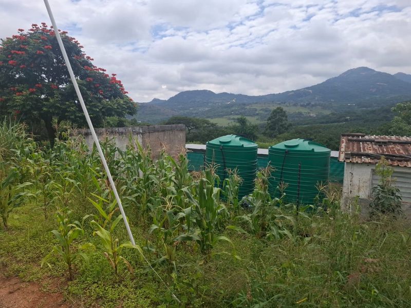 Rear farm exterior featuring water storage tanks, a masonry wall, and a structure with a weathered corrugated metal roof, set against a mountain landscape.