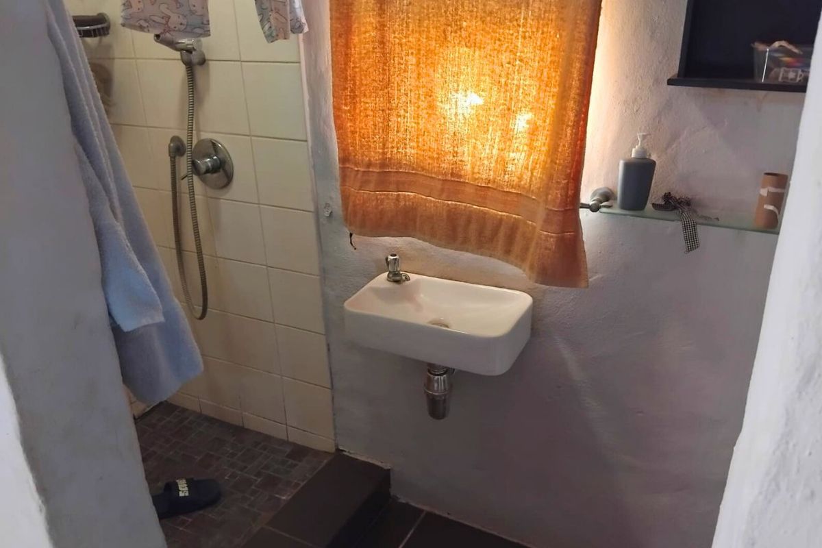 A compact bathroom featuring a wall-mounted basin and a tiled shower enclosure with a handheld shower mixer.