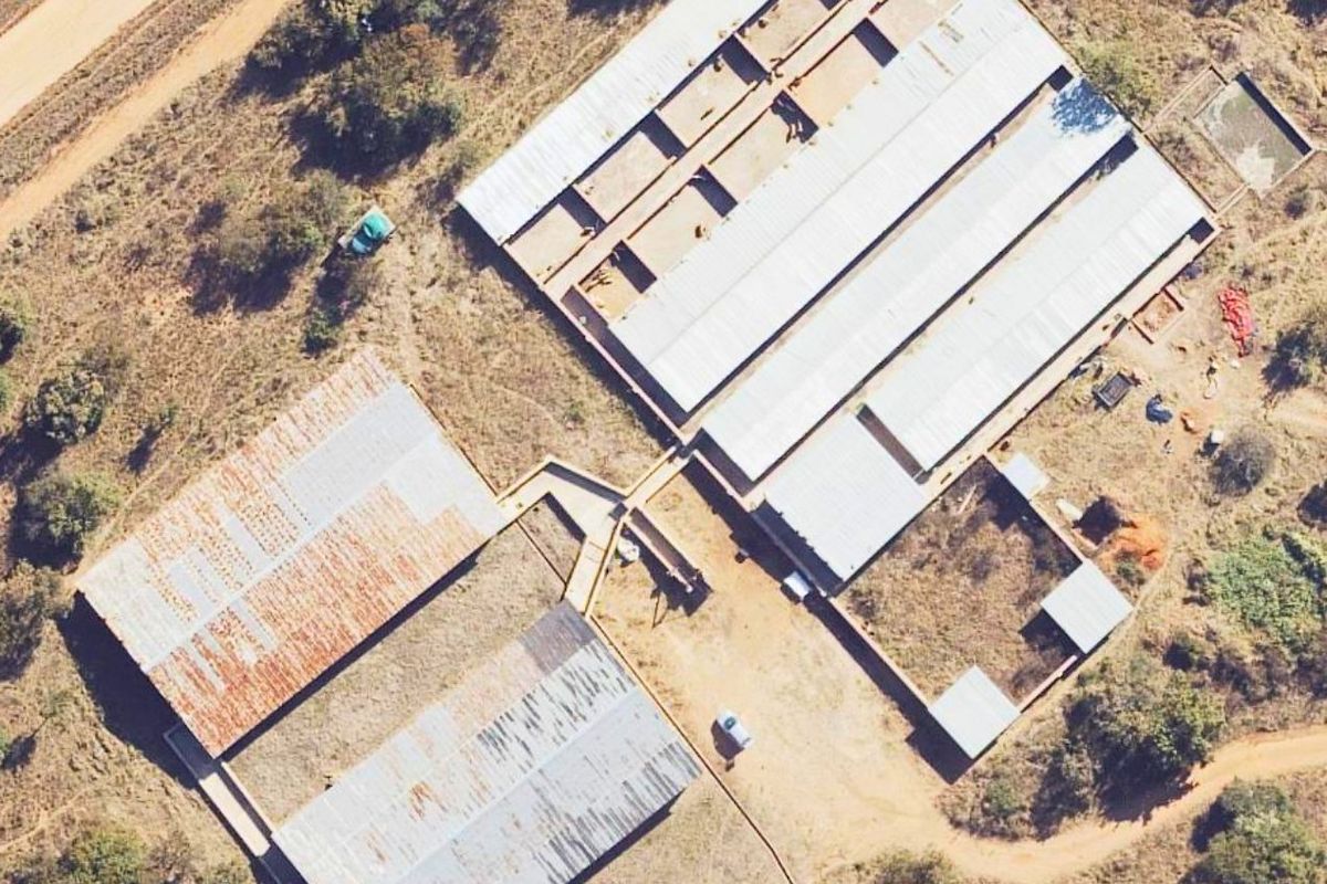 Aerial view of a farm property featuring multiple outbuildings with corrugated metal roofing and fenced enclosures set within a rural landscape.