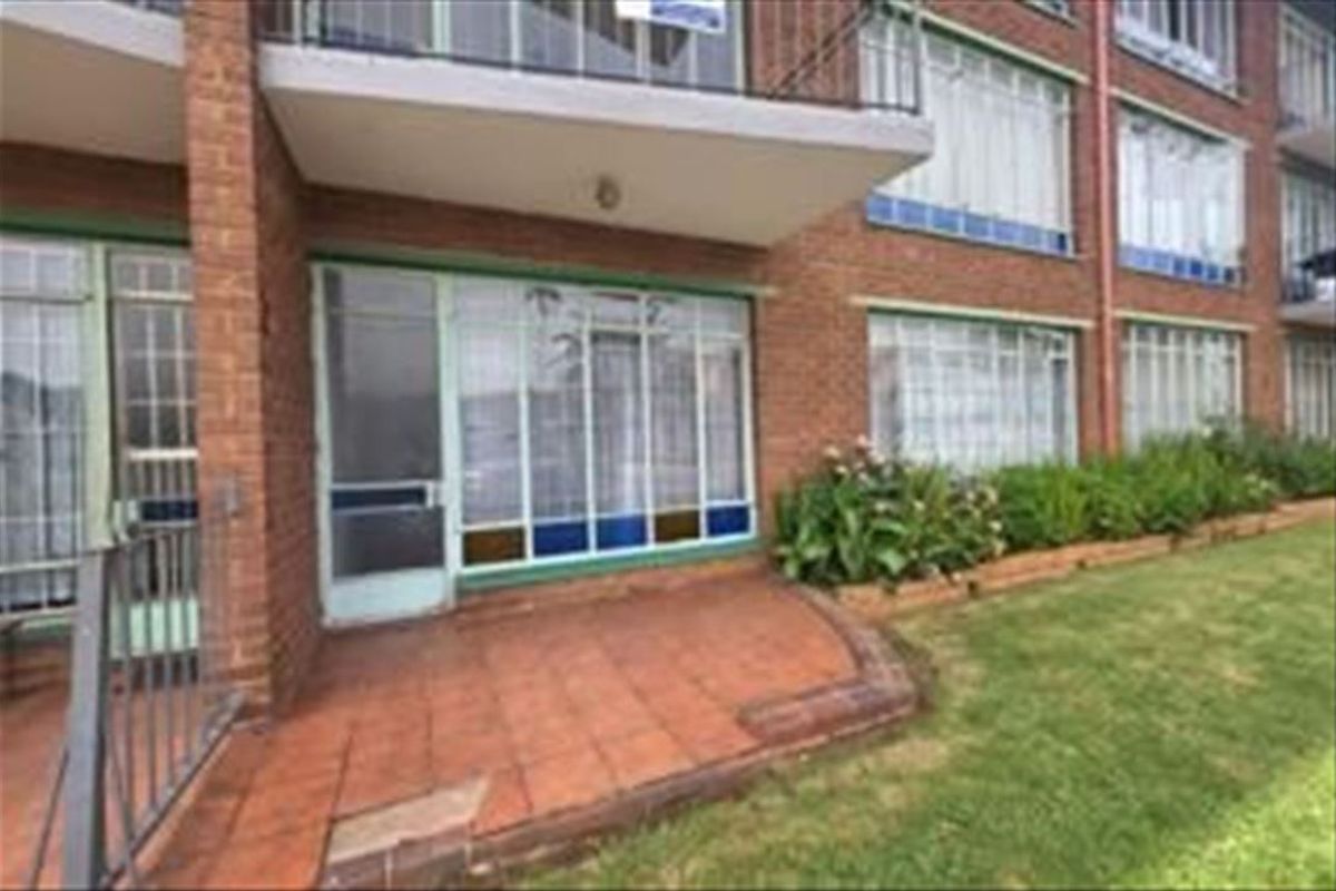 Exterior view of an apartment building featuring a ground floor tiled patio, brick facade, and metal security fixtures.