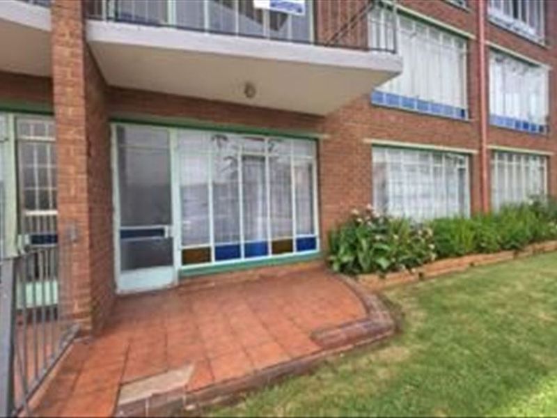 Exterior view of an apartment building featuring a ground floor tiled patio, brick facade, and metal security fixtures.