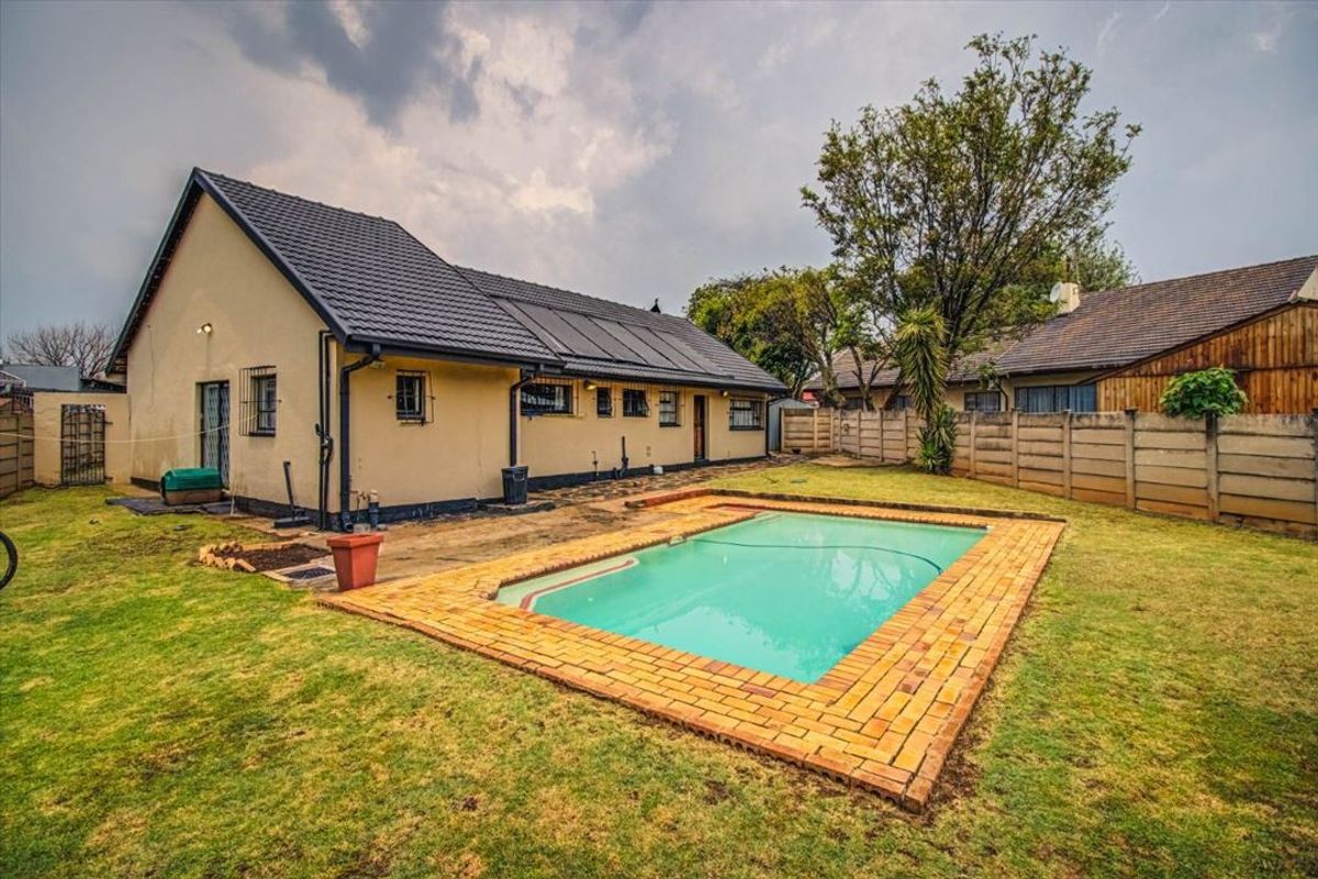 Rear garden featuring a swimming pool with brick coping, solar heating panels on the roof, and a precast concrete boundary wall.