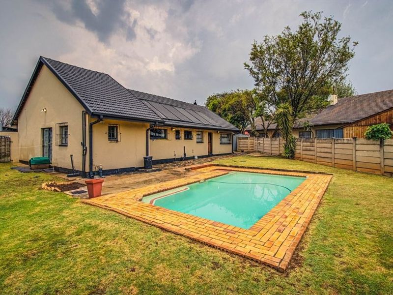 Rear garden featuring a swimming pool with brick coping, solar heating panels on the roof, and a precast concrete boundary wall.