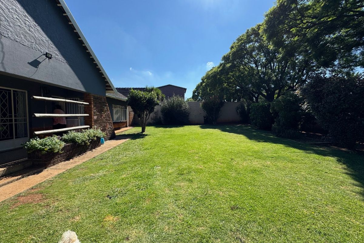 A spacious rear garden featuring a well-maintained lawn, mature trees, and a paved walkway adjacent to the house exterior.