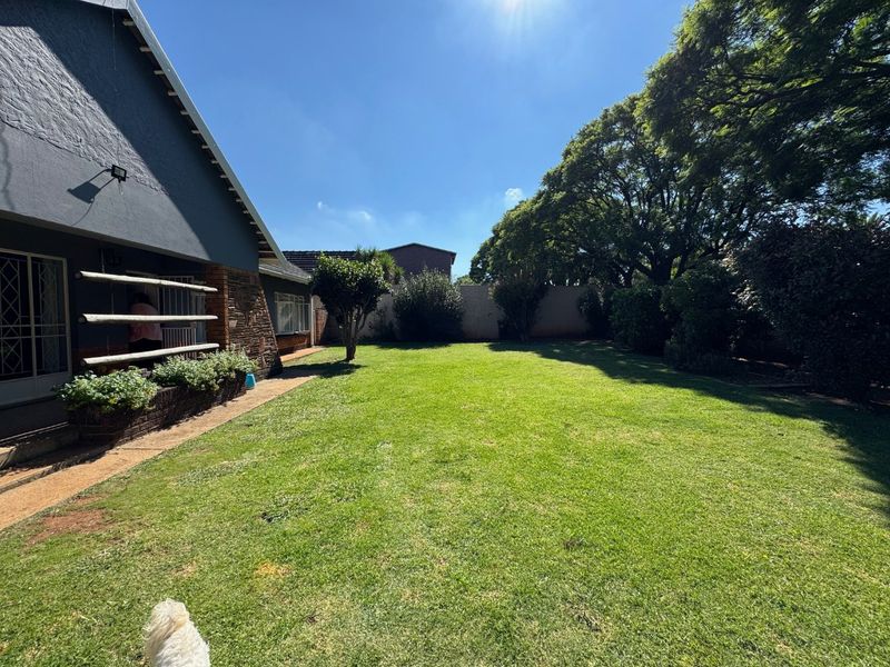 A spacious rear garden featuring a well-maintained lawn, mature trees, and a paved walkway adjacent to the house exterior.