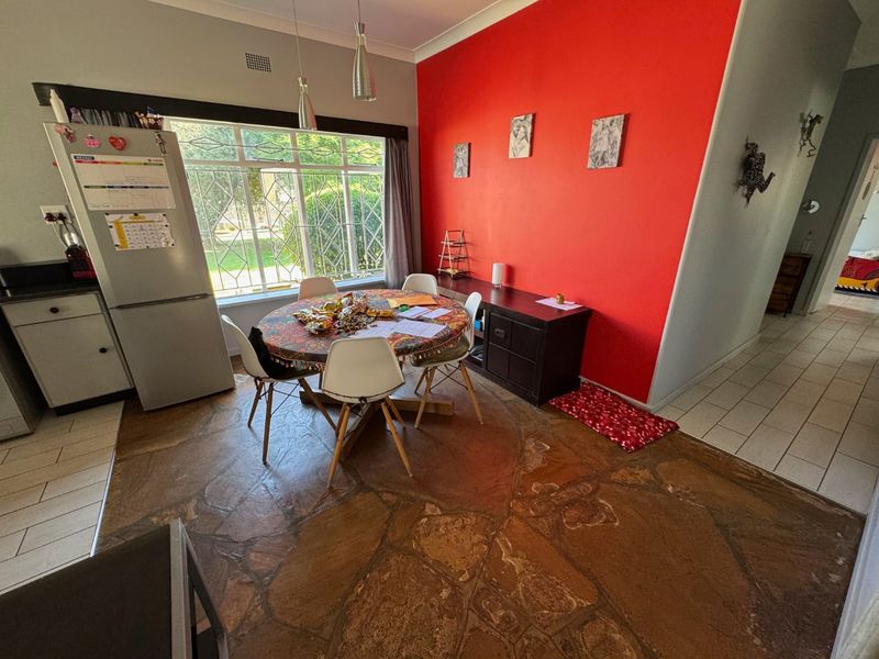Dining area featuring natural stone flooring, a large window with security bars, and a bold red accent wall.