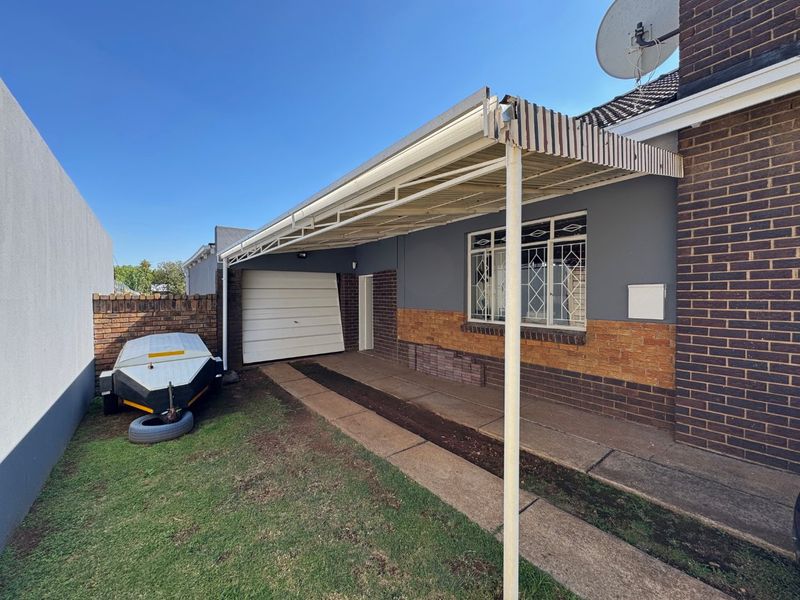 Exterior view of the property featuring a carport, brick and rendered facade, and a single garage with a damaged door.