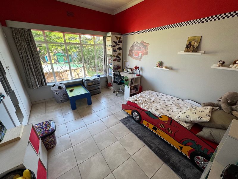 A spacious bedroom featuring large windows with security bars, tiled flooring, and built-in storage cupboards.