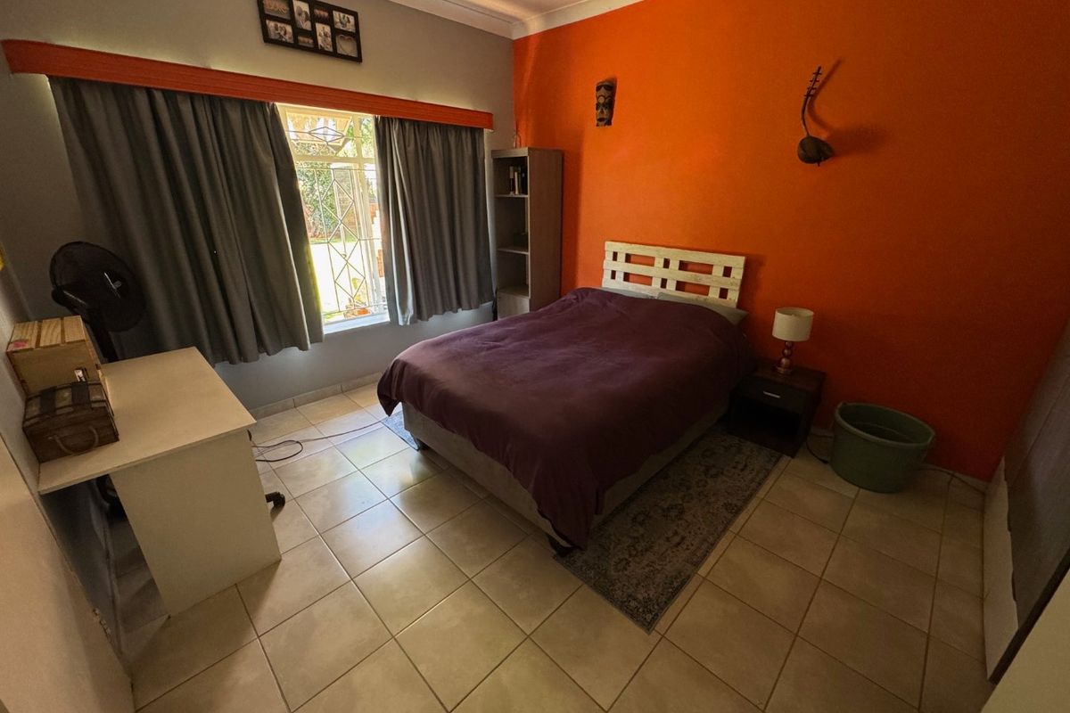 A bedroom featuring tiled flooring, a window with security bars, and a bold orange accent wall.