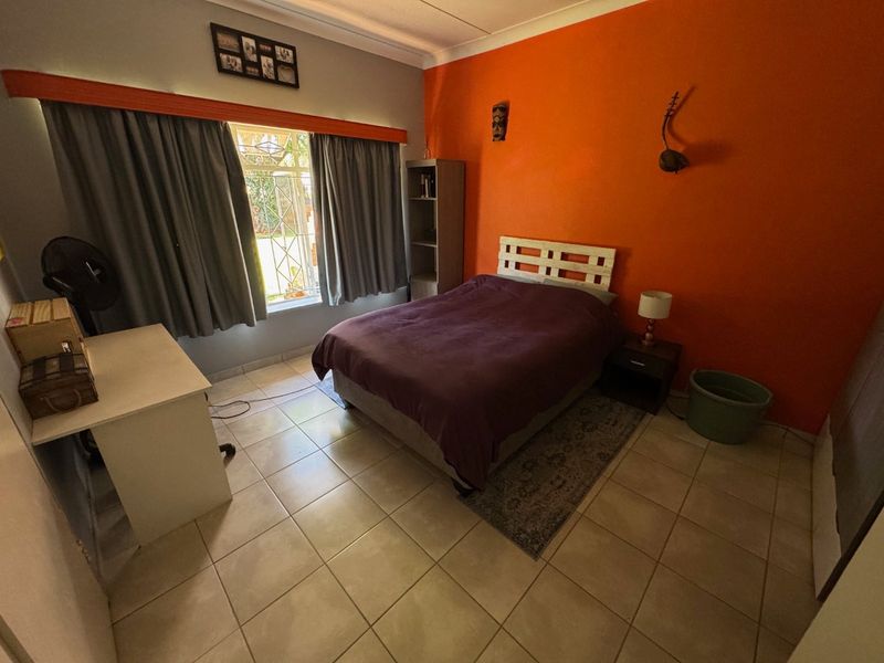 A bedroom featuring tiled flooring, a window with security bars, and a bold orange accent wall.
