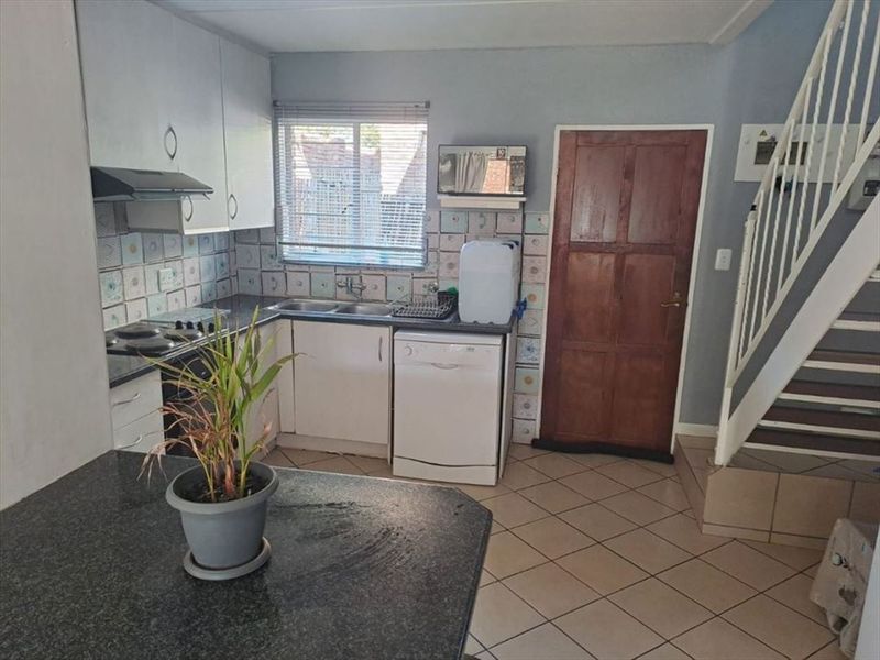 Functional kitchen featuring built-in cabinetry, laminate countertops, a double basin sink, and tiled flooring, with an adjacent staircase.