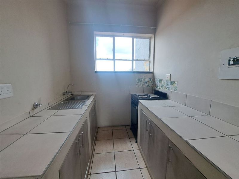 A functional galley-style kitchen featuring tiled countertops, built-in cabinetry, a stainless steel sink, and a freestanding stove.