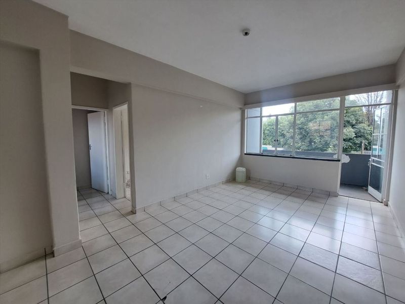 A spacious, empty living area featuring neutral tiled flooring, large windows providing natural light, and direct access to an outdoor balcony.