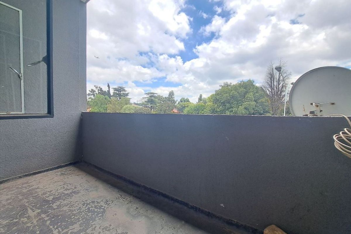 A private balcony featuring a solid wall enclosure and an open view of the surrounding neighborhood and trees.