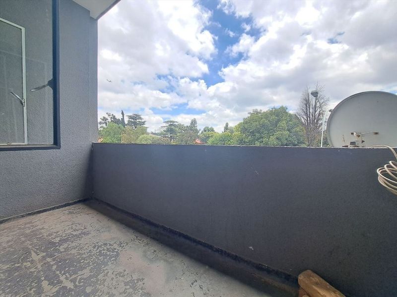A private balcony featuring a solid wall enclosure and an open view of the surrounding neighborhood and trees.