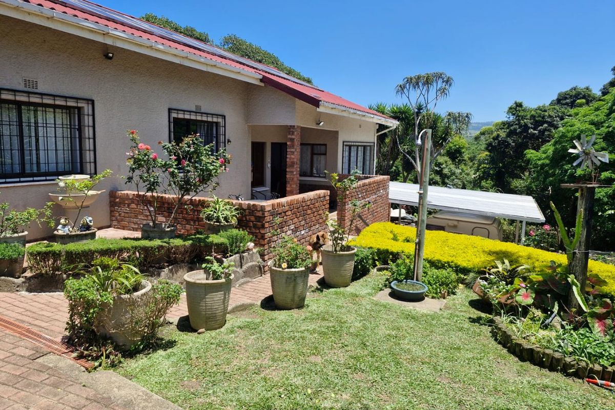 A view of the rear exterior of the house featuring a brick patio area, landscaped garden, and a covered carport structure.