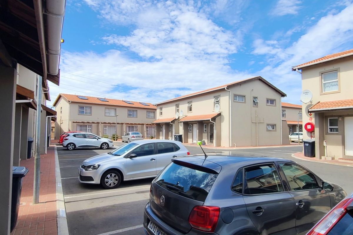 A view of a residential complex courtyard featuring paved parking areas and multi-story townhouse units with tiled roofs.