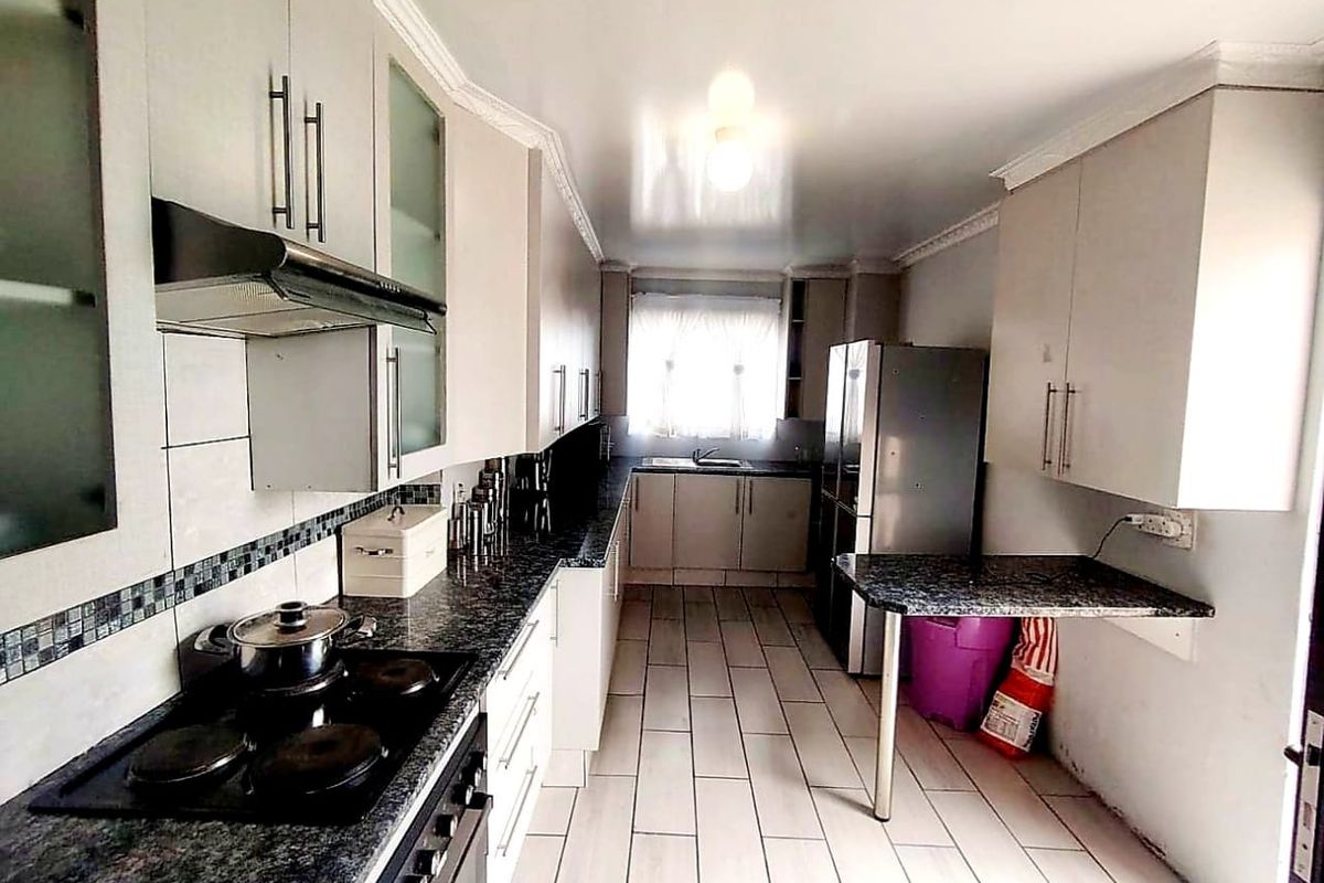 A functional kitchen featuring granite countertops, ample built-in cabinetry, an electric hob with extractor, and a convenient breakfast bar area.