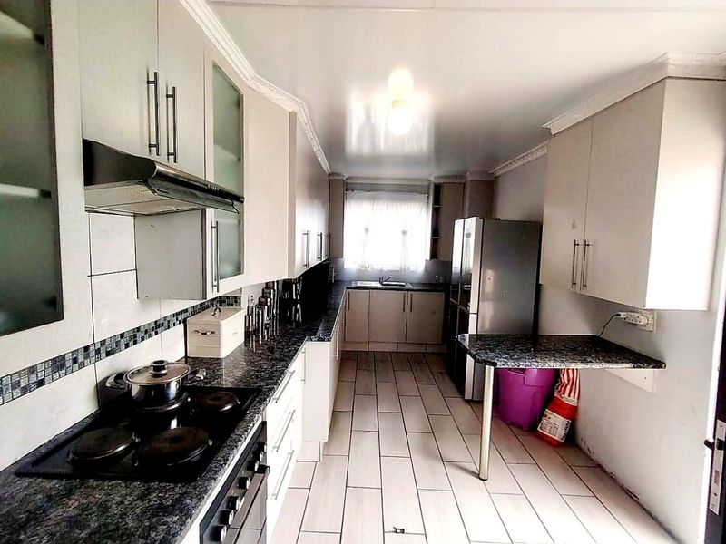 A functional kitchen featuring granite countertops, ample built-in cabinetry, an electric hob with extractor, and a convenient breakfast bar area.