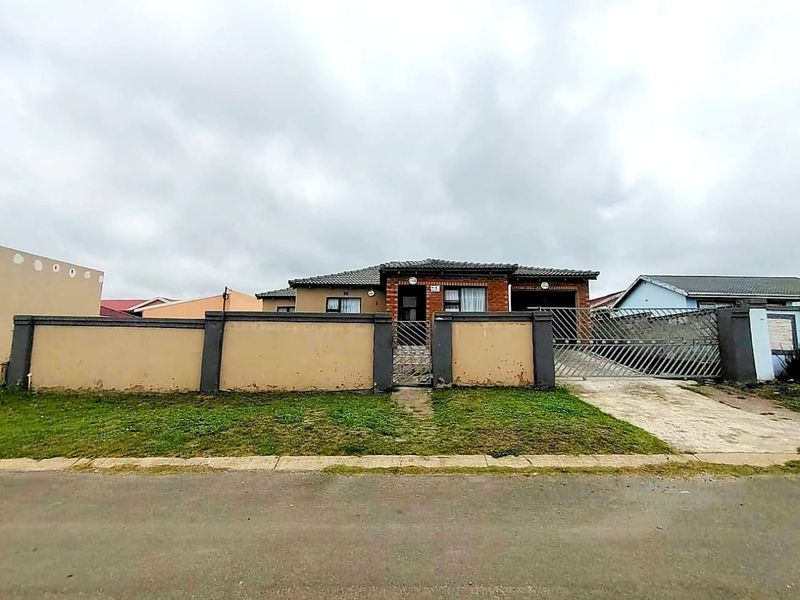 Front view of a single-story residential house featuring a brick facade, tiled roof, concrete driveway, and a gated perimeter wall.