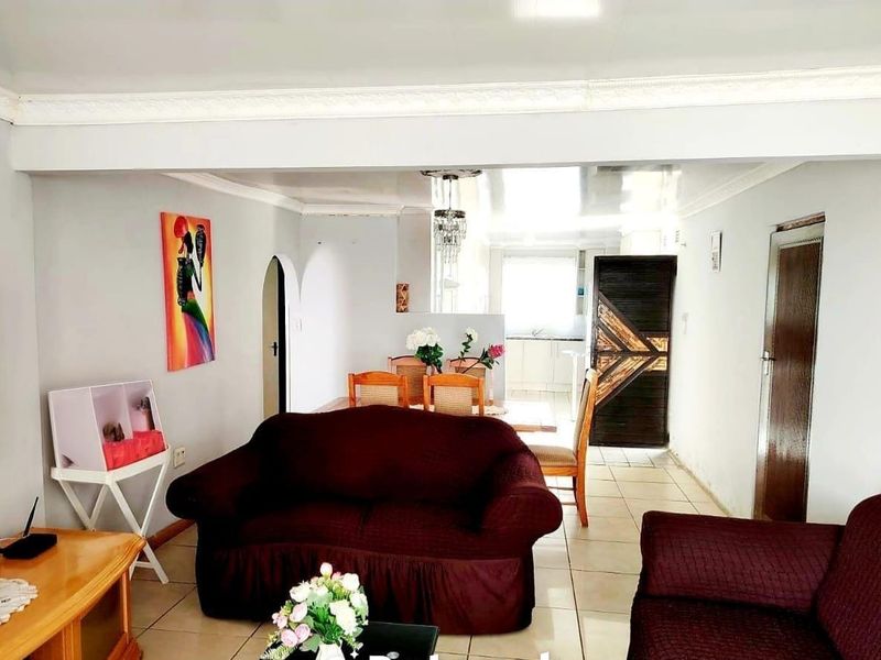 Open plan living and dining area featuring tiled floors, decorative ceiling cornices, and a central chandelier, connecting to the kitchen space.