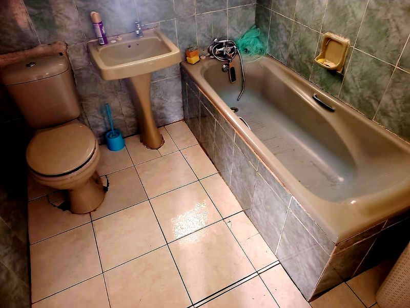 A dated bathroom featuring a pedestal basin, bathtub, and toilet with tiled finishes, requiring cosmetic updates and repairs to the flooring.
