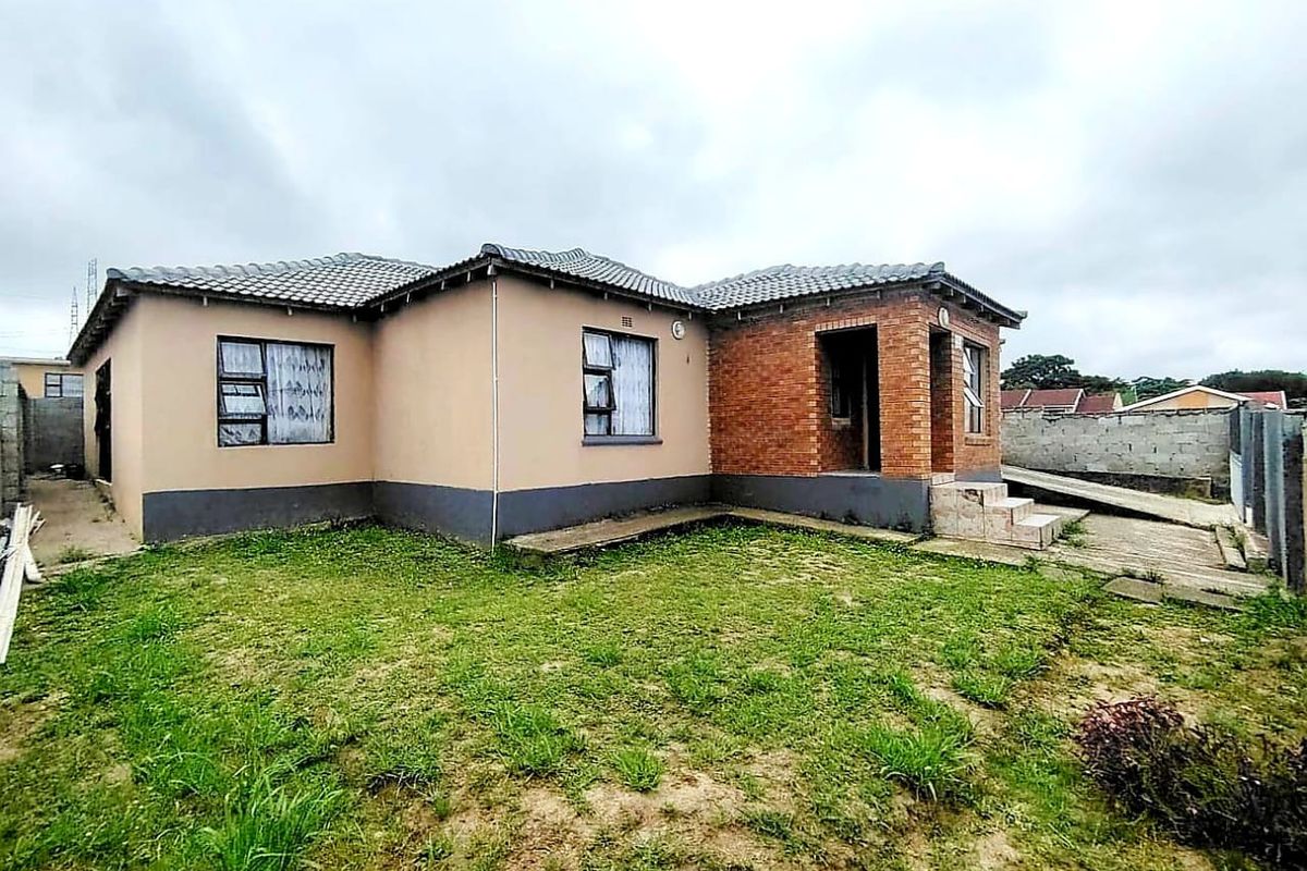 Rear view of a single-story house featuring a combination of brick and plastered exterior walls, a tiled roof, and a concrete driveway.