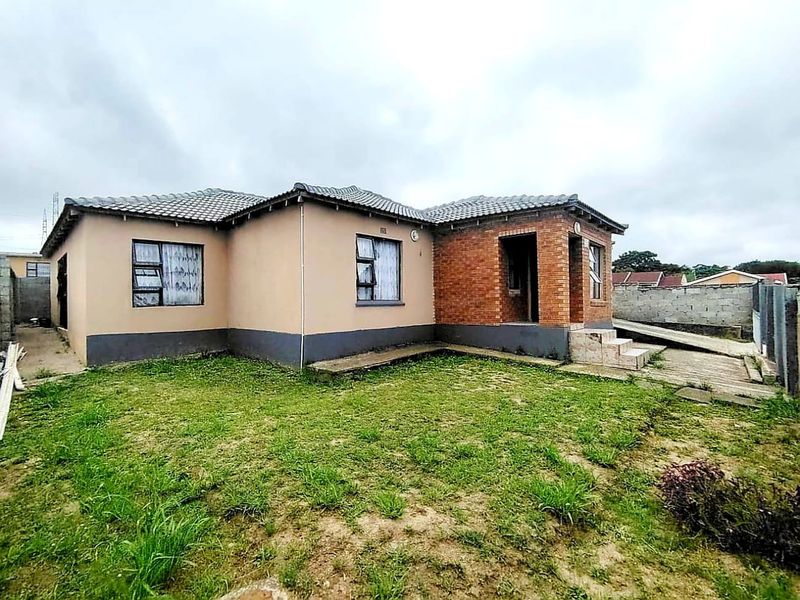 Rear view of a single-story house featuring a combination of brick and plastered exterior walls, a tiled roof, and a concrete driveway.