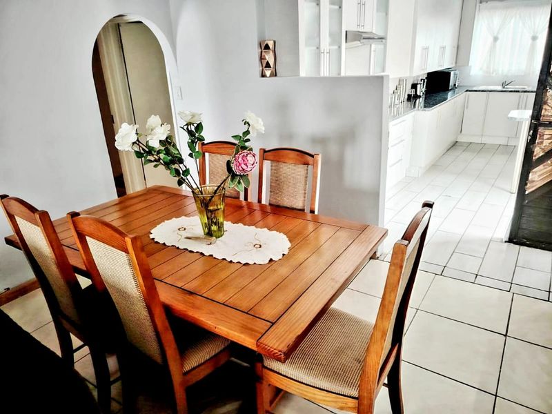 Open-plan dining area flowing into a modern kitchen with white cabinetry, granite countertops, and tiled flooring throughout.