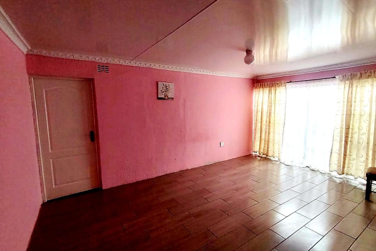 An empty living room featuring tiled flooring, a sliding glass door providing natural light, and decorative ceiling cornicing.