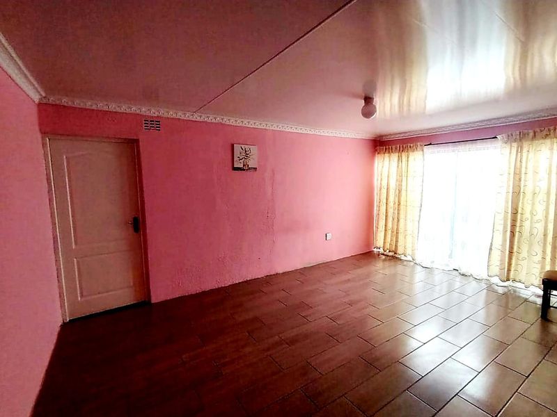 An empty living room featuring tiled flooring, a sliding glass door providing natural light, and decorative ceiling cornicing.