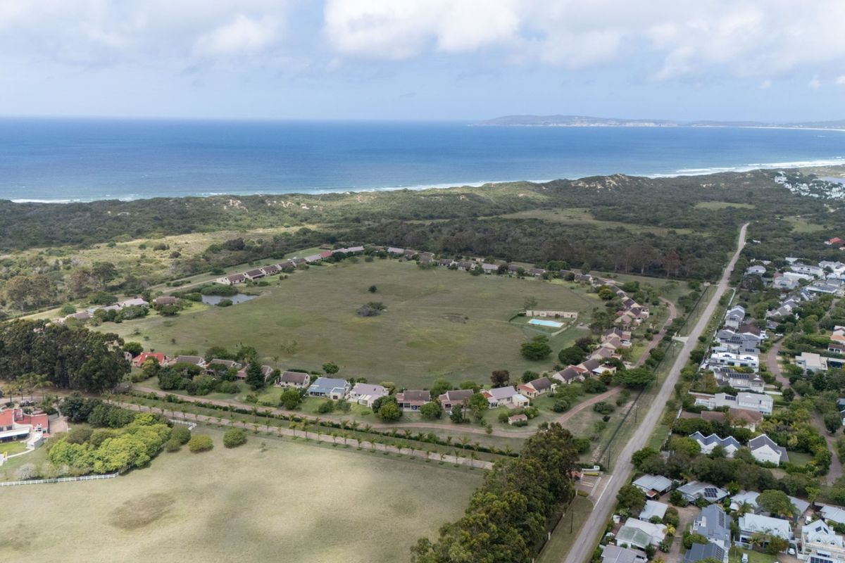 An aerial view of a residential estate featuring a central green space, surrounding houses, and proximity to the coastline.