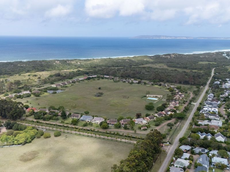 An aerial view of a residential estate featuring a central green space, surrounding houses, and proximity to the coastline.