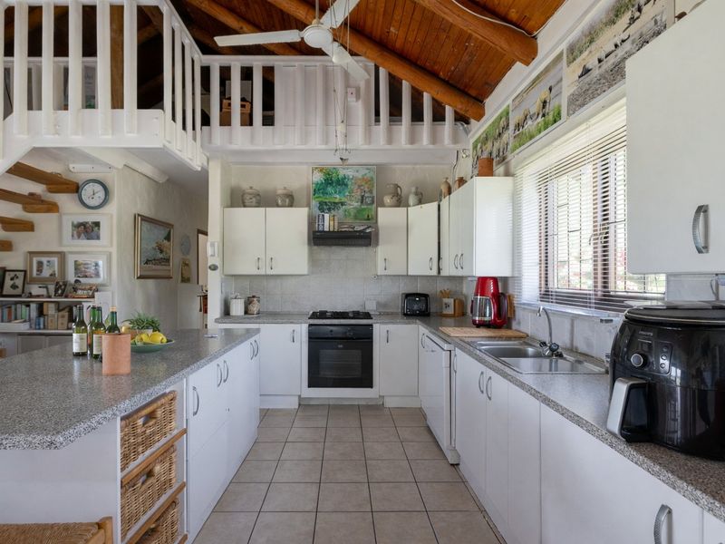 Open-plan kitchen featuring white cabinetry, granite countertops, integrated oven and hob, and a mezzanine level with wooden ceiling beams.