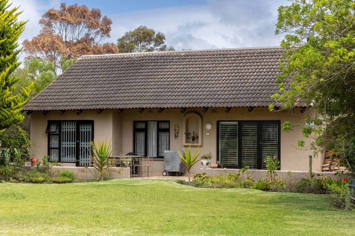 Rear view of a single-story house featuring a tiled roof, stucco exterior, and multiple glass doors opening onto a garden patio area.