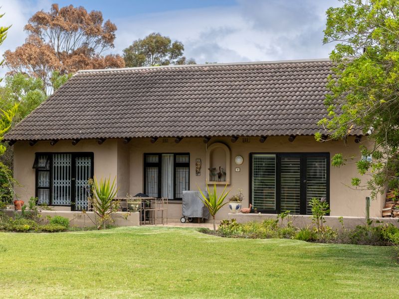 Rear view of a single-story house featuring a tiled roof, stucco exterior, and multiple glass doors opening onto a garden patio area.