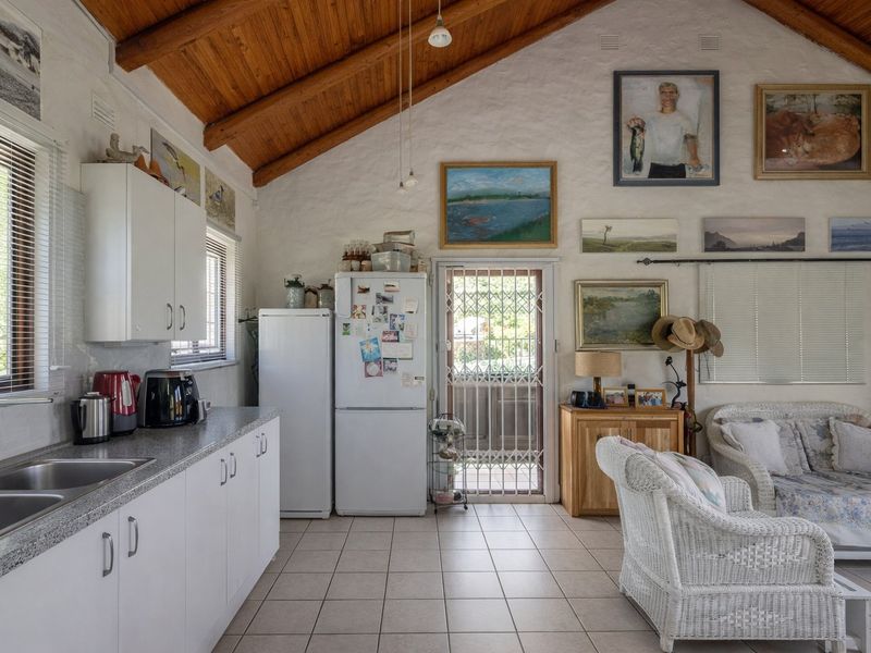 Open-plan kitchen and living area featuring vaulted timber ceilings, tiled flooring, and direct access to the exterior through a security gate.