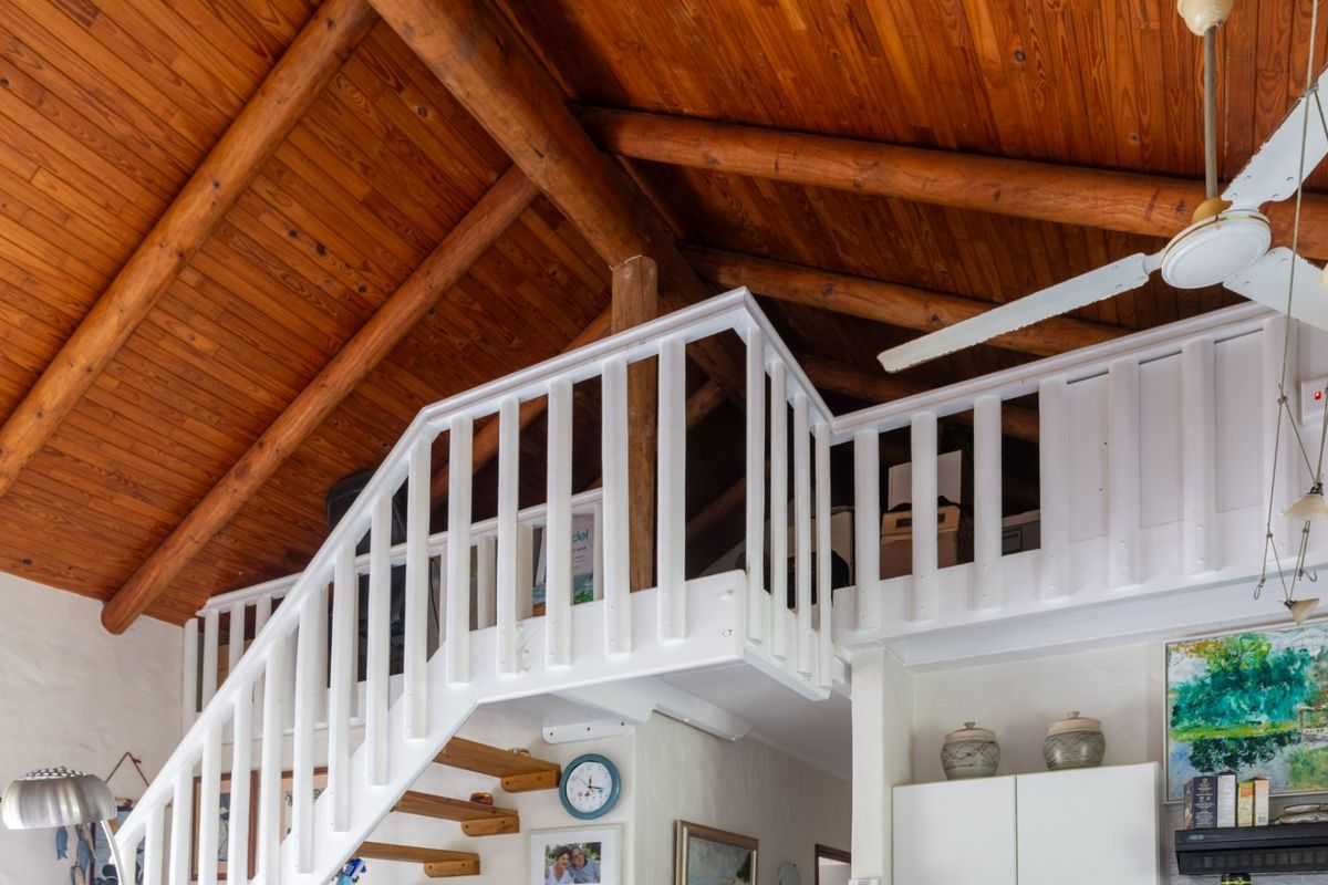 A mezzanine level featuring a wooden vaulted ceiling with exposed beams and a white balustrade, accessed by a staircase.