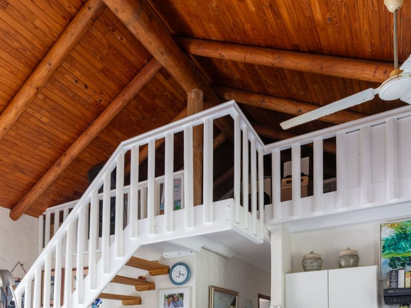 A mezzanine level featuring a wooden vaulted ceiling with exposed beams and a white balustrade, accessed by a staircase.