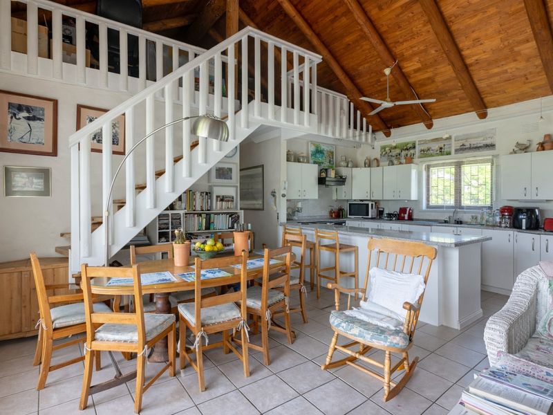 Open-plan living and kitchen area featuring a mezzanine level, exposed timber ceiling beams, tiled flooring, and a central kitchen island with breakfast bar.