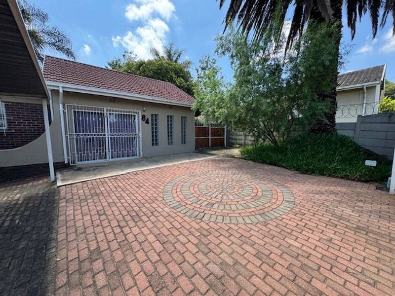 Front exterior view of the property featuring a paved driveway with a circular pattern, security gates, and a tiled roof structure.