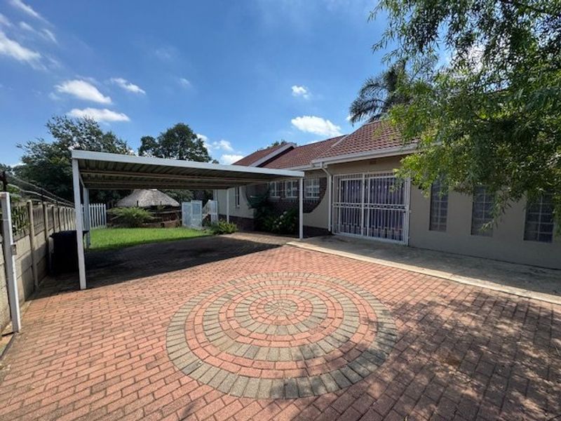 A paved driveway area featuring a covered carport, brick facade, and security gates, providing functional off-street parking and access to the property.