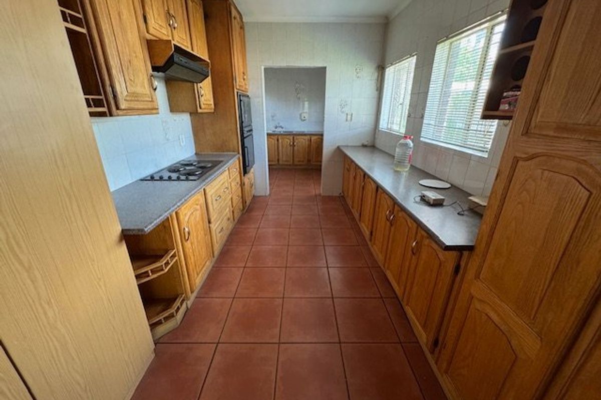 A functional galley-style kitchen featuring timber cabinetry, tiled flooring, built-in hob, and an integrated oven, with an adjoining scullery area.
