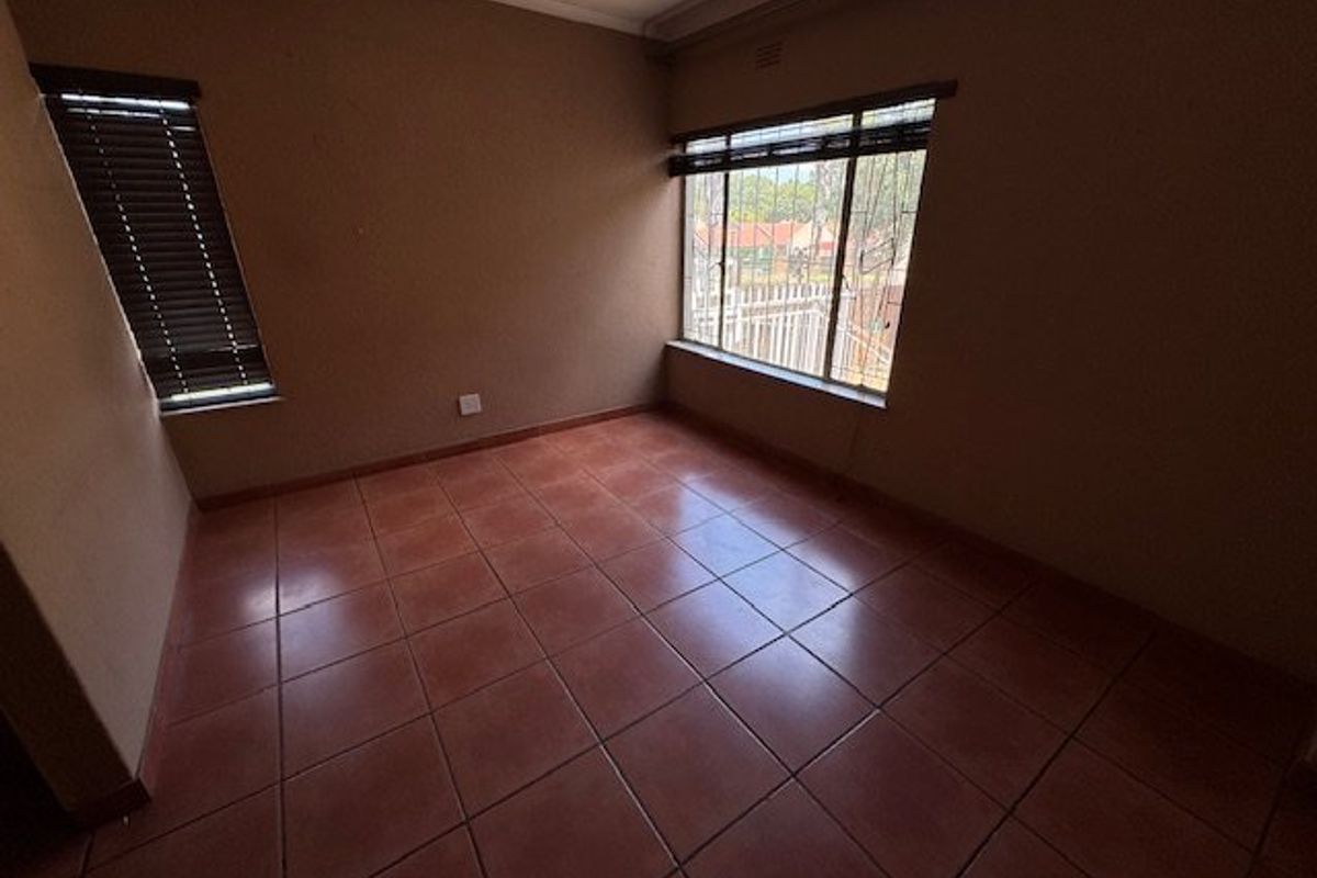 A vacant bedroom featuring terracotta floor tiles, neutral wall paint, and fitted window blinds.